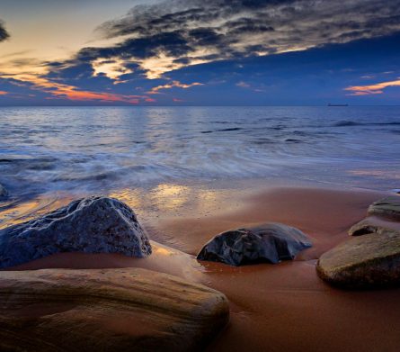 A beach with rocks and water at sunset